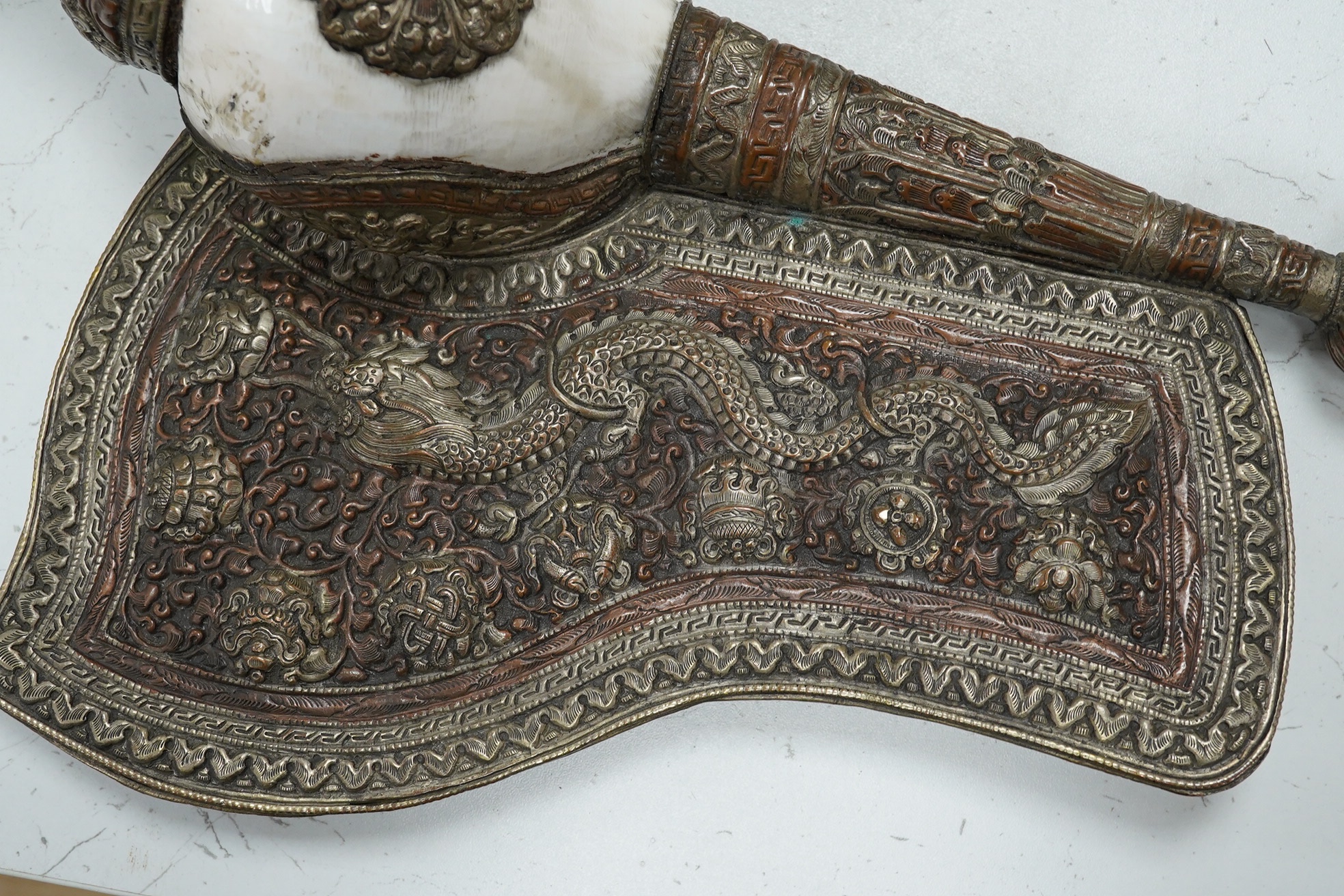 A Tibetan repoussé work cowrie shell trumpet, early 20th century, set with a cabochon, 37cm high. Condition - fair to good